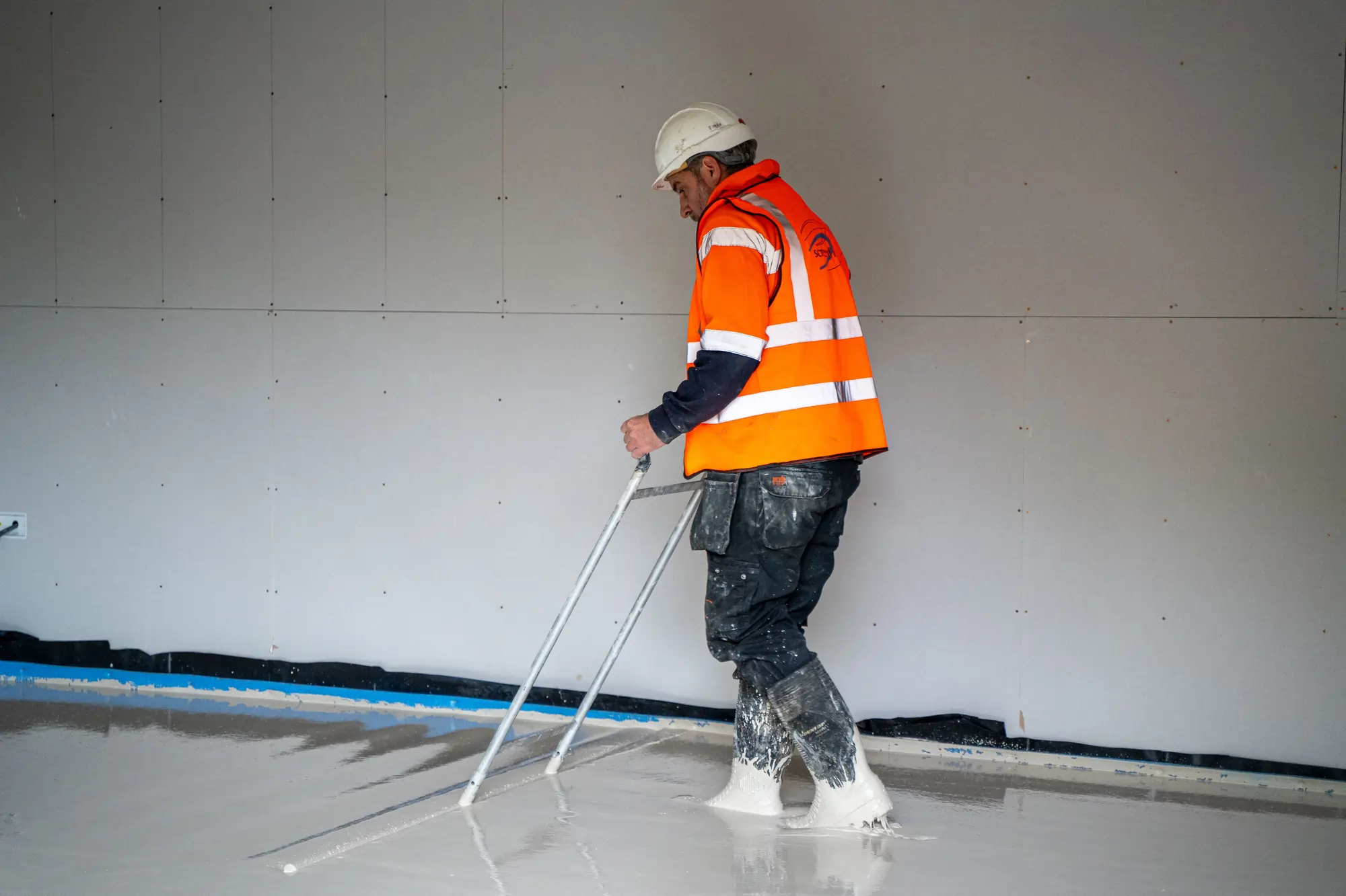 Man using paddle bars to settle screed wearing orange high vis