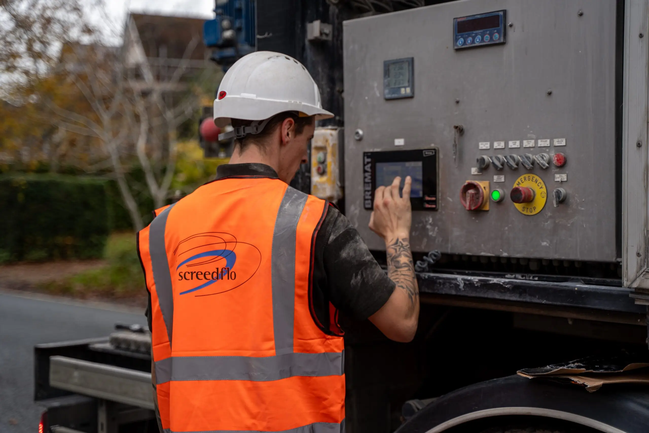 man wearing orange high vis with screedflo lorry touching buttons on a bremat lorry