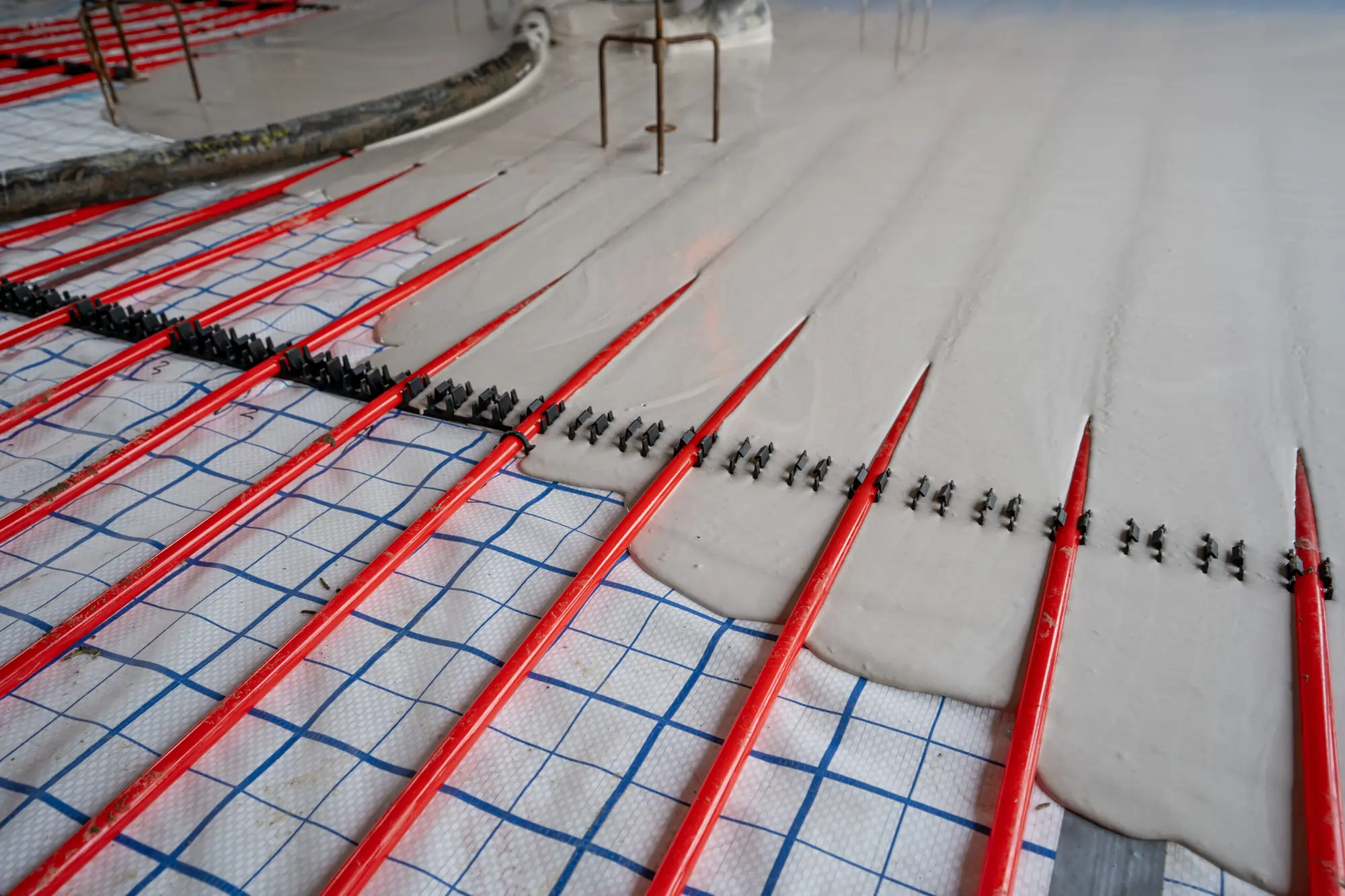 Red underfloor heating pipes with liquid screed pouring over it.